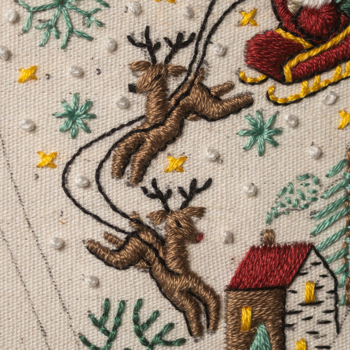 May include: Embroidered image of Santa Claus in a red sleigh pulled by two reindeer flying over a snowy landscape with a small house in the background.