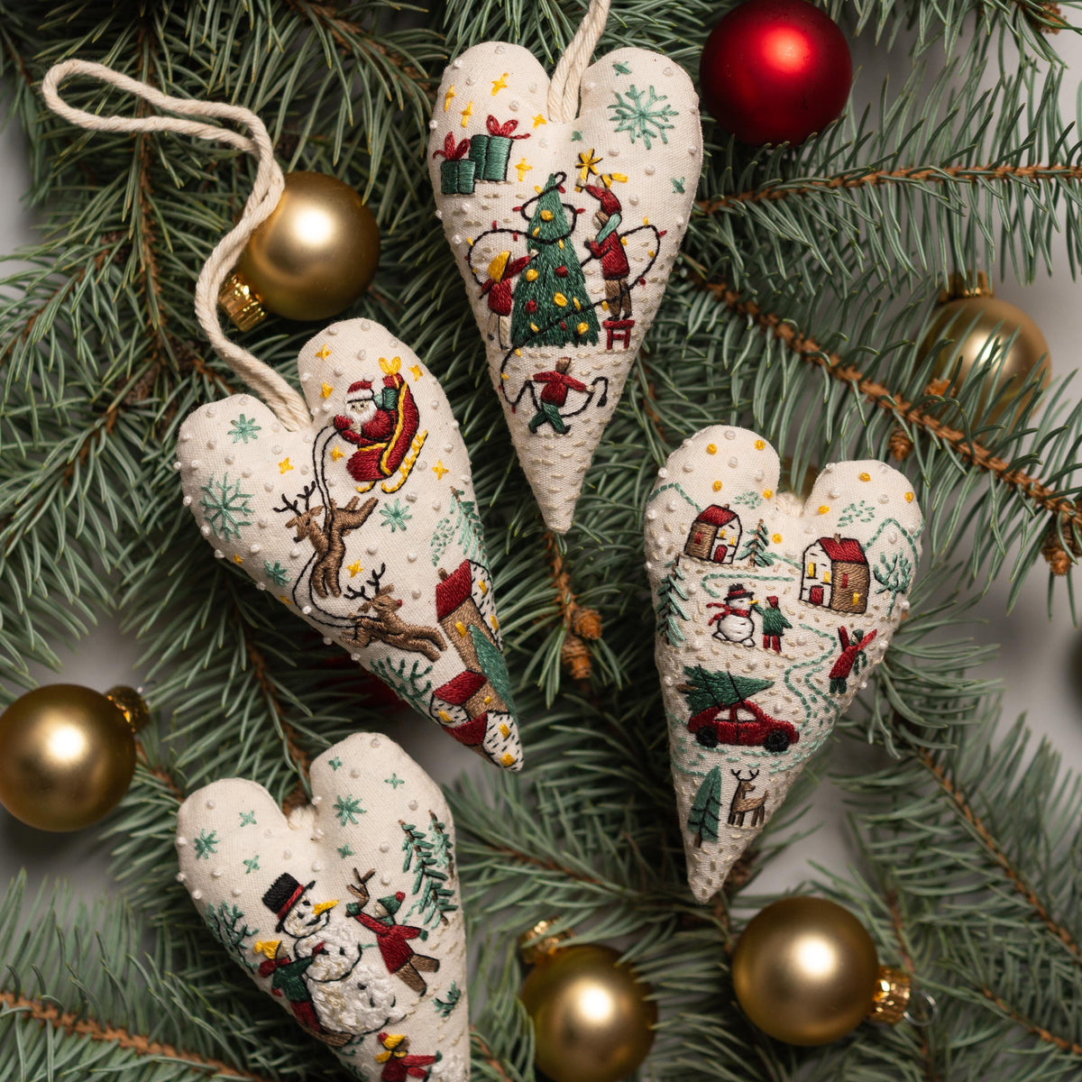 May include: Four handmade heart-shaped ornaments with embroidered Christmas scenes. The ornaments feature a white background with green, red, and yellow details. The scenes include a Christmas tree, Santa Claus in a sleigh, a snowman, and a winter v
