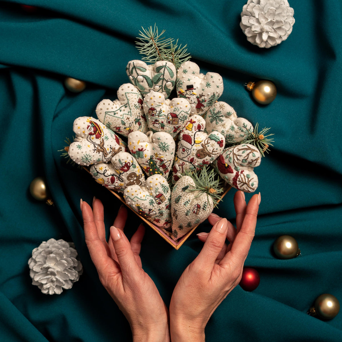 May include: A collection of handmade felt heart ornaments with various winter-themed embroidery designs, displayed in a wooden box. The ornaments are arranged in a heart shape and feature a variety of colors, including red, green, white, and brown.