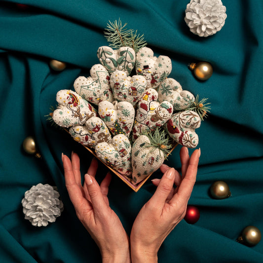 May include: A collection of handmade felt heart ornaments with various winter-themed embroidery designs, displayed in a wooden box. The ornaments are arranged in a heart shape and feature a variety of colors, including red, green, white, and brown.