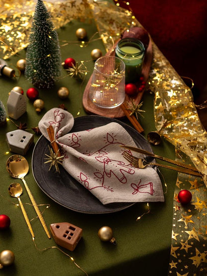 May include: A festive Christmas table setting with a green tablecloth, featuring a decorated napkin, gold cutlery, and red and gold ornaments. A small Christmas tree and miniature houses add to the holiday theme.