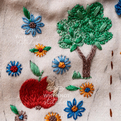 May include: A beige fabric featuring hand embroidery of a large green tree with a brown trunk, a red apple with a green leaf, and various small flowers in blue, yellow, and brown. The text "WHY KNOT" is embroidered in white thread.