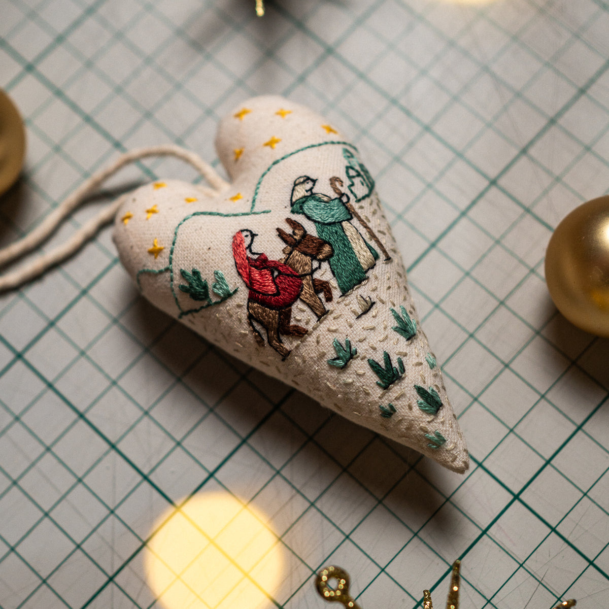 Close-up of a finished embroidered Christmas heart ornament depicting Mary, Joseph, and their donkey traveling toward Bethlehem.