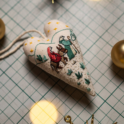 Close-up of a finished embroidered Christmas heart ornament depicting Mary, Joseph, and their donkey traveling toward Bethlehem.
