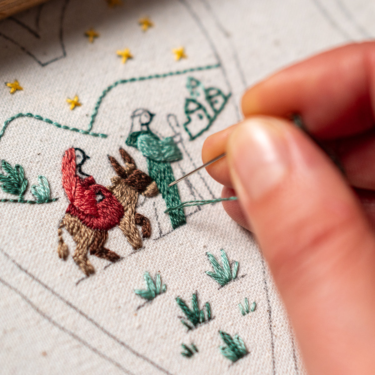 Close-up of hand embroidery in progress, showing Mary on the donkey and Joseph being stitched on The Road to Bethlehem Christmas heart pattern.