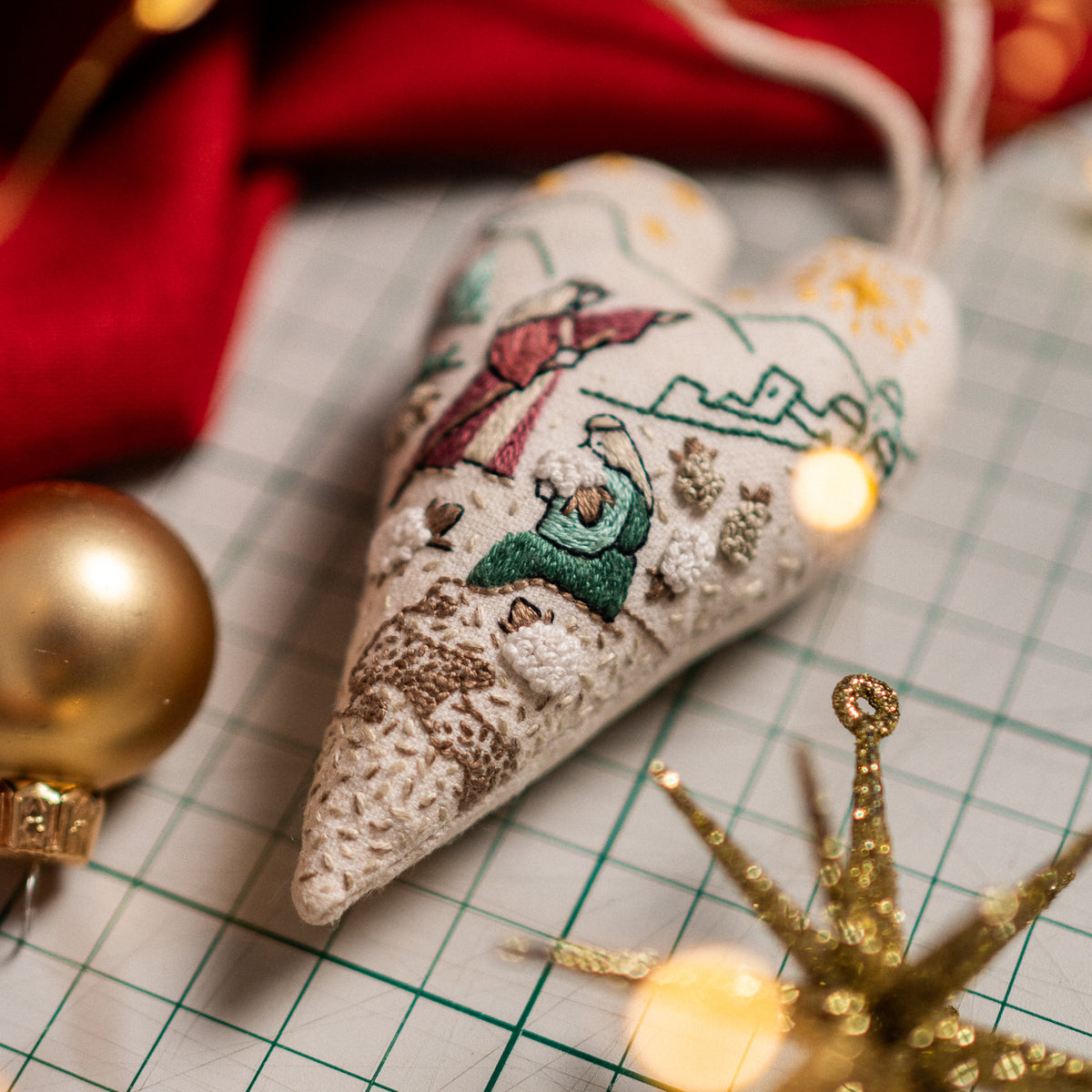 Finished Shepherds of Bethlehem Christian Christmas heart ornament with embroidered shepherds and sheep, styled with golden baubles and festive star decorations.